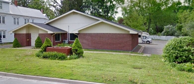 A single-storey brick building sits on a road with grass and trees at the front.