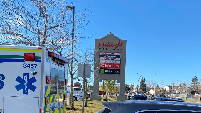 An ambulance and a car parked in front of a strip mall sign.