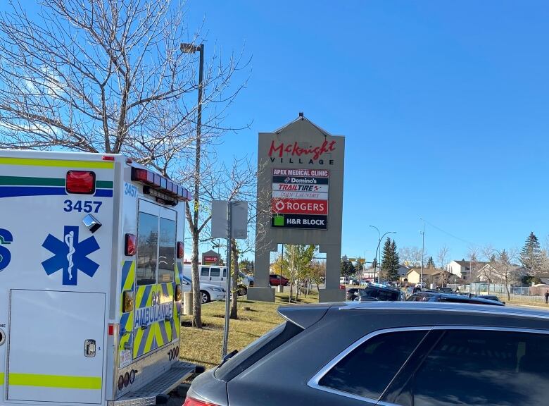 An ambulance and a car parked in front of a strip mall sign.