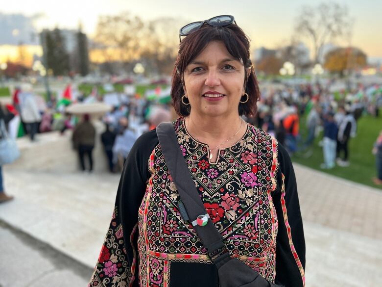 A woman stands with a shoulder bag. 