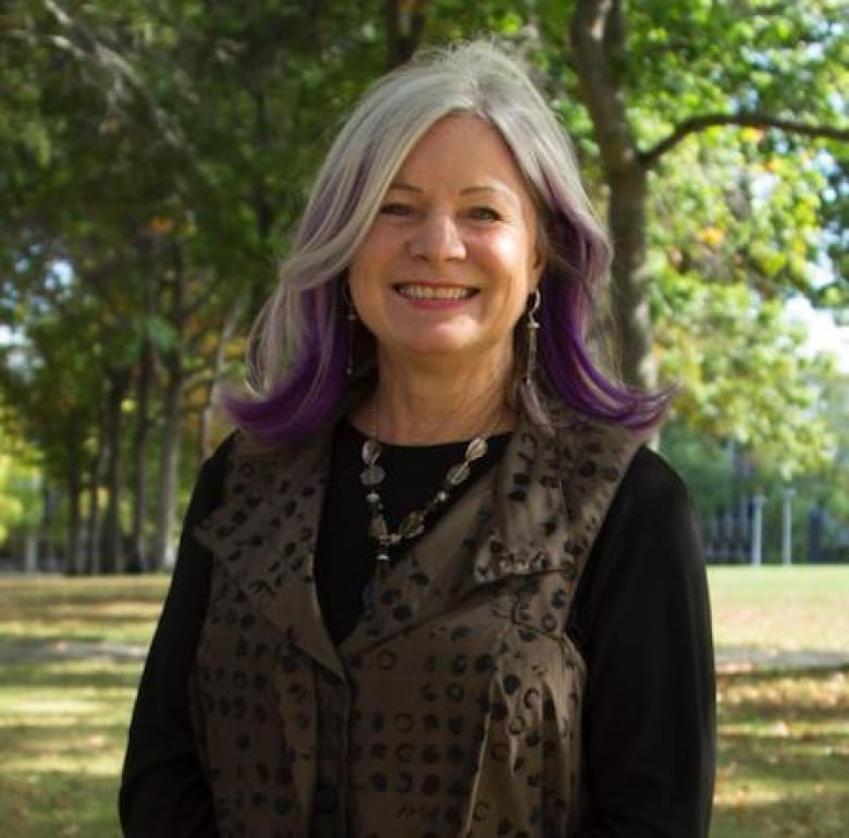 A woman with purple hair extensions smiles in an outdoor environment.