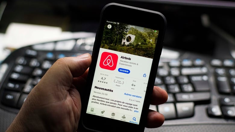 A man holds up a cell phone with the Airbnb App Store blurb visible in French.