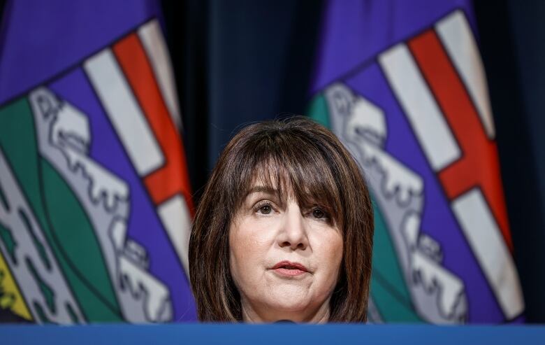 A woman with brown hair with an Alberta flag in the background. 