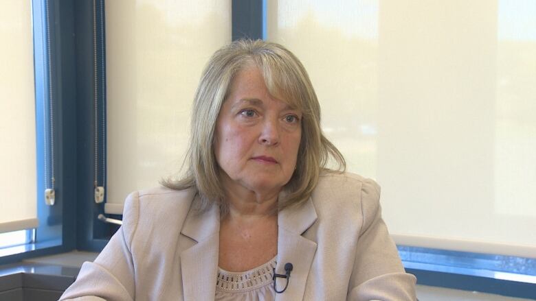 A woman wearing a grey blazer sits at a table in a boardroom.