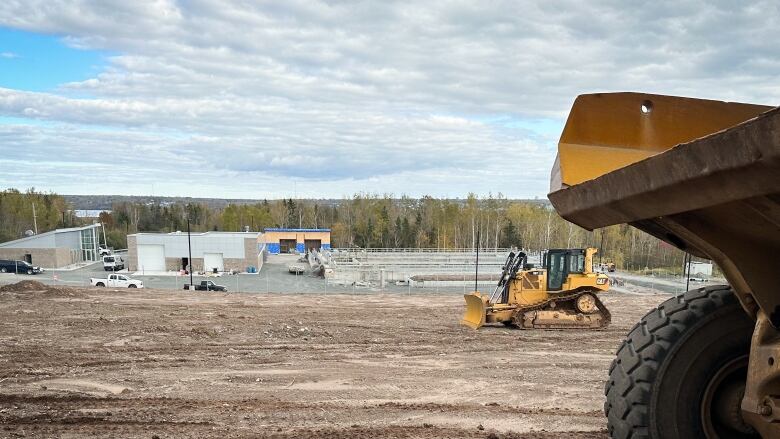 A dump truck and bulldozer sit on a muddy field in front of a new building.