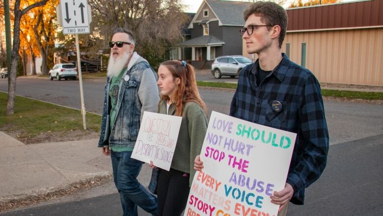 Three people carry signs against gender-based violence.