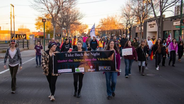 A group of people walk carrying signs for take back the night.