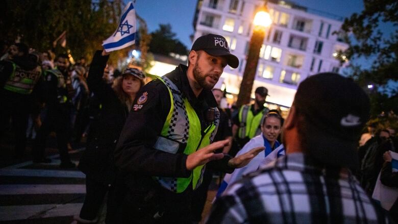 A police officer speaks to a protestors with some people holding Israeli flags behind him.