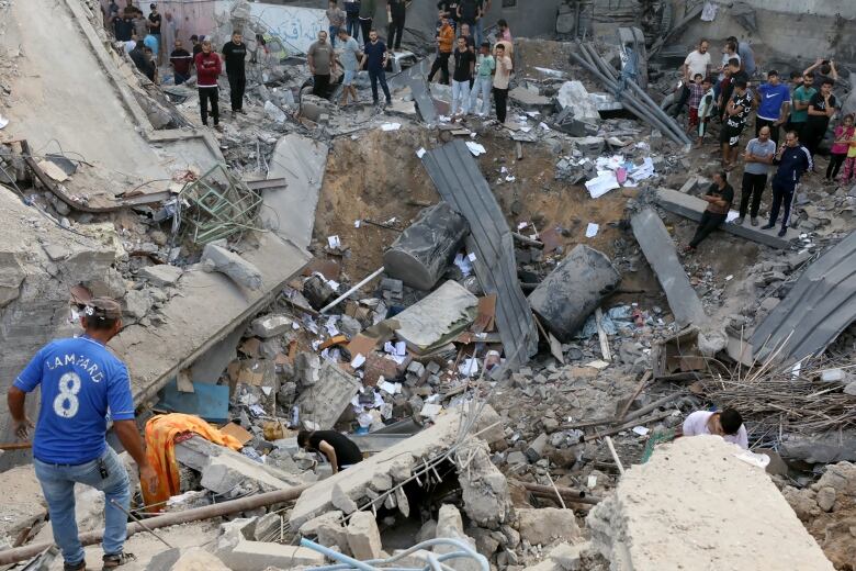 A crater filled with pieces of concrete and debris is shown, with several people standing around it.