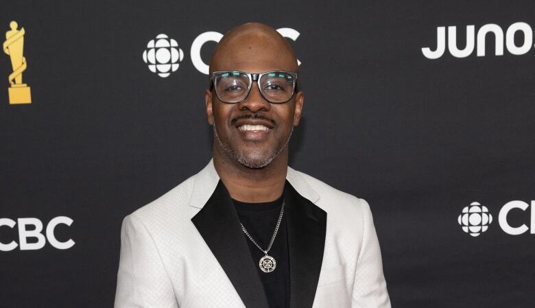 A man in a white blazer and black slacks poses on a red carpet.