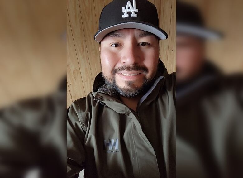 A man with dark hair wears a baseball cap with the LA logo. He smiles at the camera