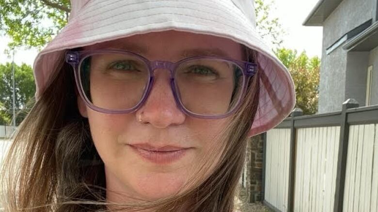 Jessy Roos wears glasses and a pink sun hat as she looks directly into the camera.