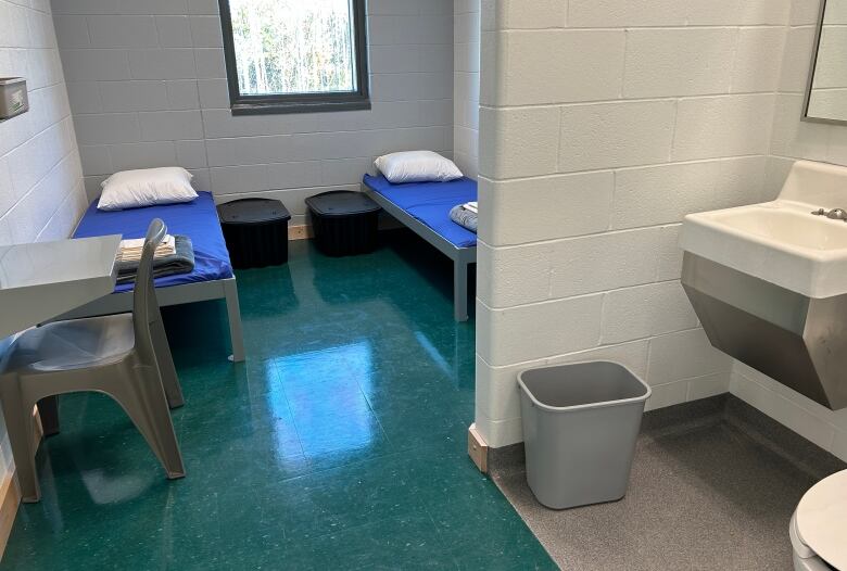 Cell with two small beds, two chairs and desks, and a sink and toilet.