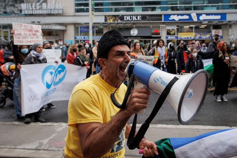 A man yells into a megaphone with protesters around him in downtown Toronto.