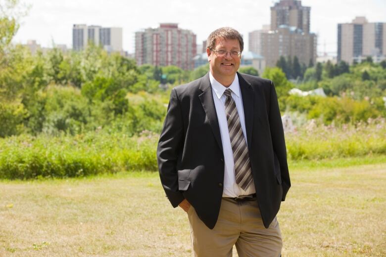 A man stands on a grassy field with buildings behind him. 