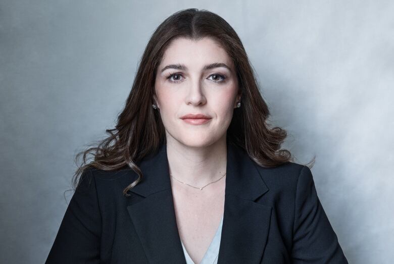 A woman in a blazer sits with her wrists crossed over each other on a table.