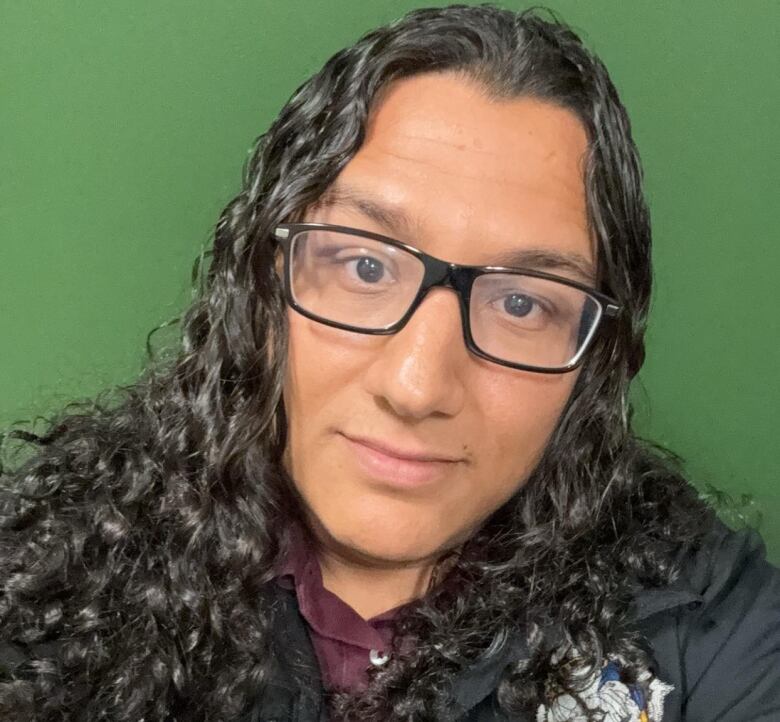 An Indigenous man wears glasses and long wavvy hair