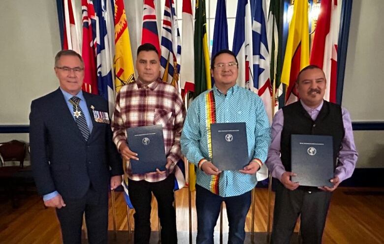 Three men in dress shirts hold certificates next to man in suit.