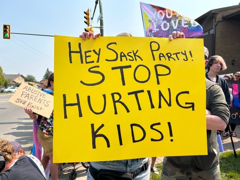 A person in a crowd holds a yellow sign reading 