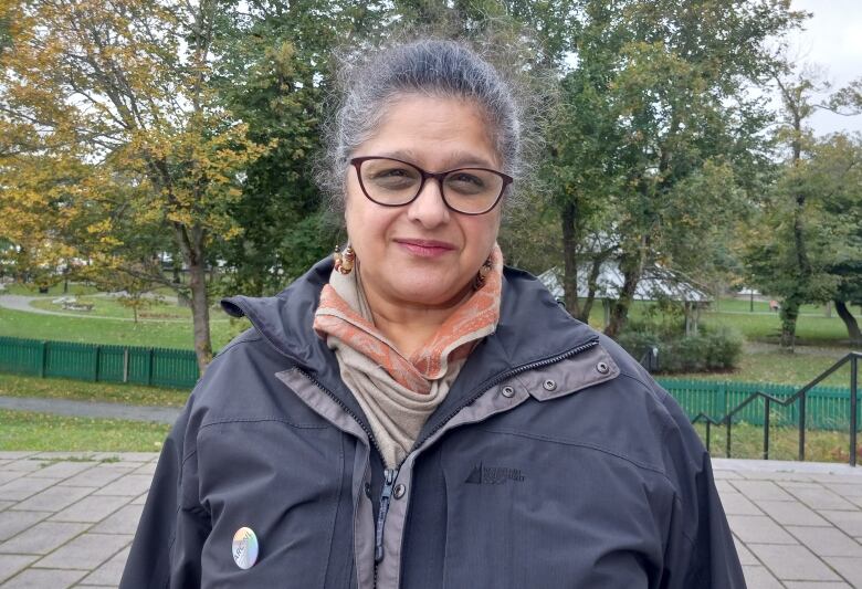 Woman in grey coat standing in front of trees