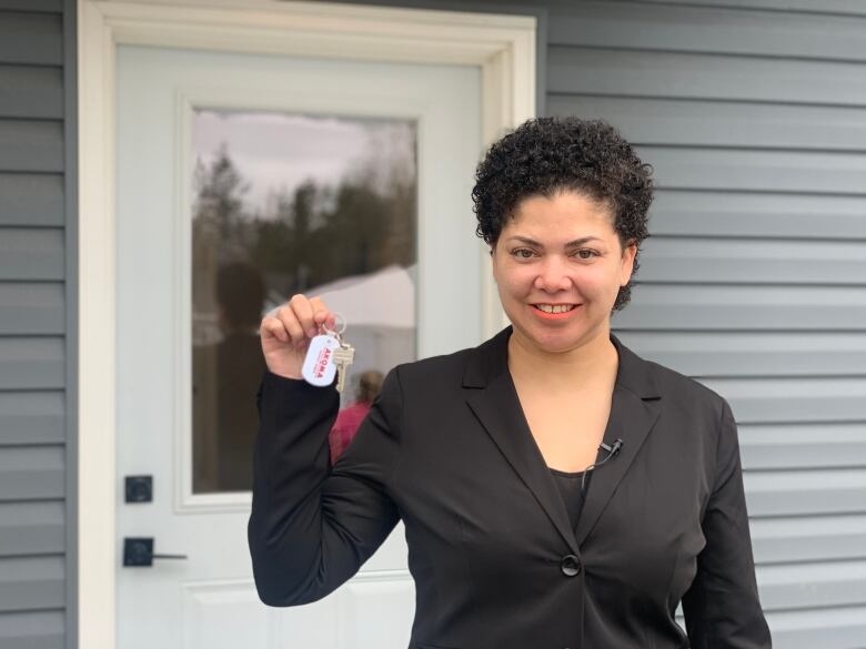 A woman holds up a set of house keys in front of a door.