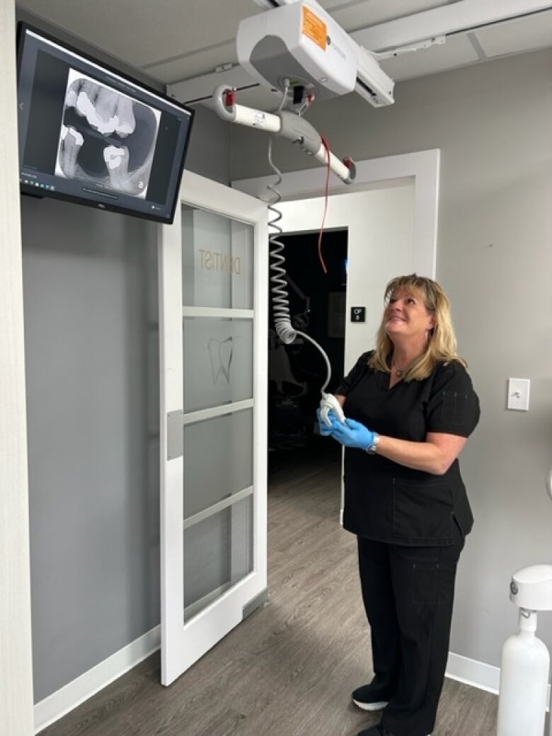 A woman holds a remote control connected to a cord that goes to the ceiling. A lift mechanism can be seen attached to the ceiling.