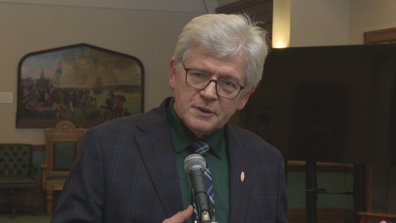 A man with a tie talks to a camera with a microphone in front of him.