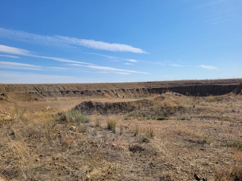 A gravel pit - a hole in the ground. Bare earth. Sparse grass growing on it.  