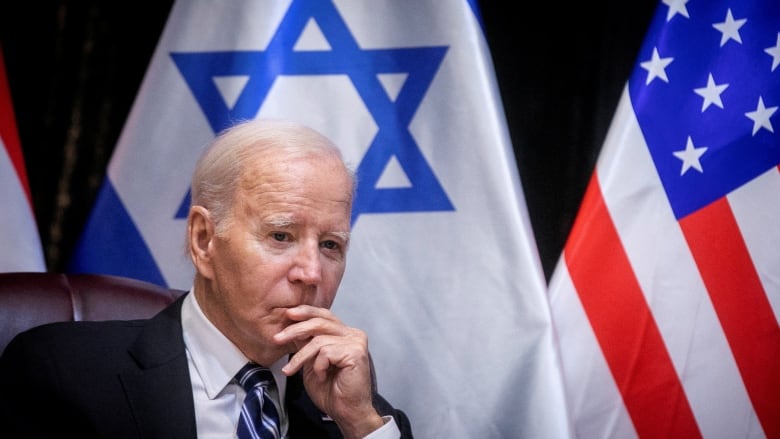 Biden, hand on chin, sits in front of Israeli and U.S. flags