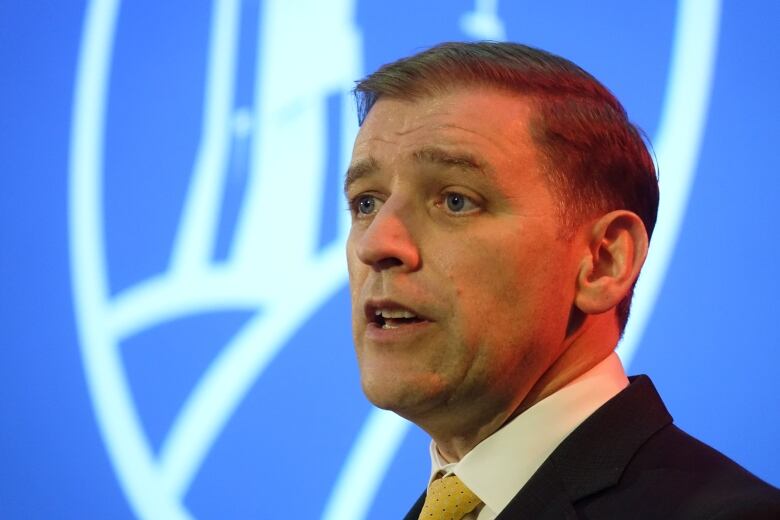 An up-close picture of a man speaking in front of a blue screen.