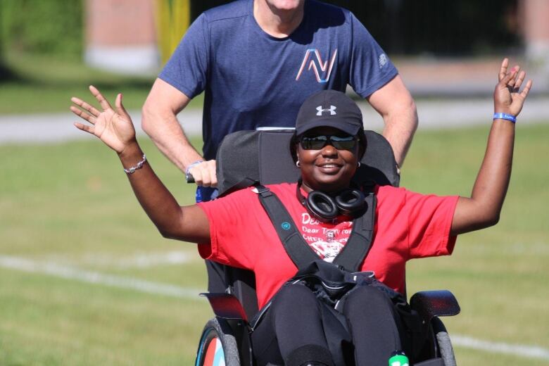 A woman sits in a wheelchair with her arms up, a man pushes the wheelchair.