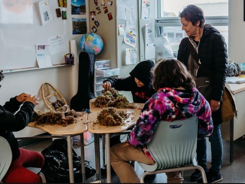 A small group of young Cree high school students sit around a table with piles of sphagnum moss, learning its traditional uses.