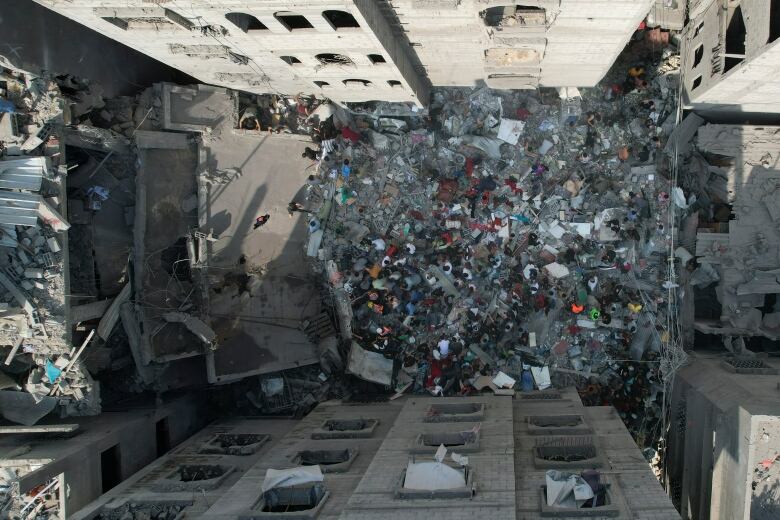 An overhead view shows people standing in the rubble of destroyed buildings.