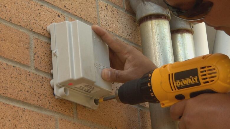 A drill is fastening a device to a brick wall.