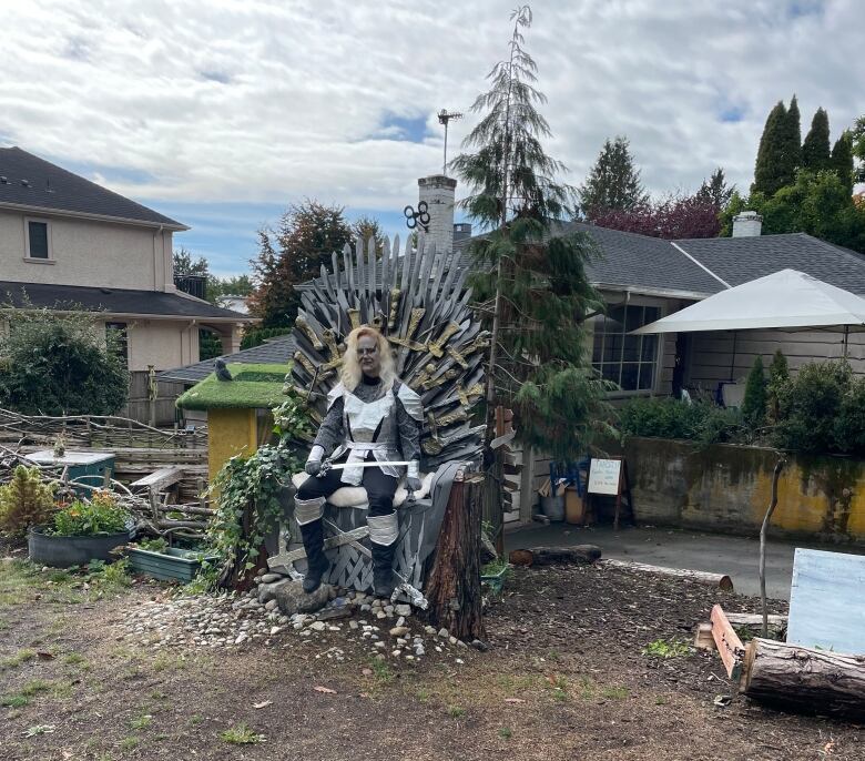 A woman is seen dressed up as a character with makeup and is sat on a throne on a driveway.