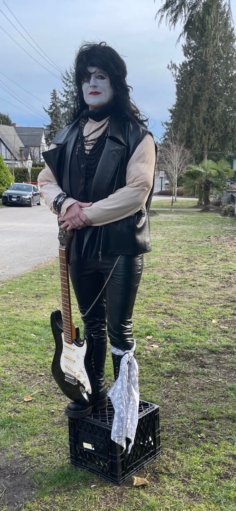 A woman dressed as Kiss guitarist Paul Stanley, with white facepaint and holding a guitar.