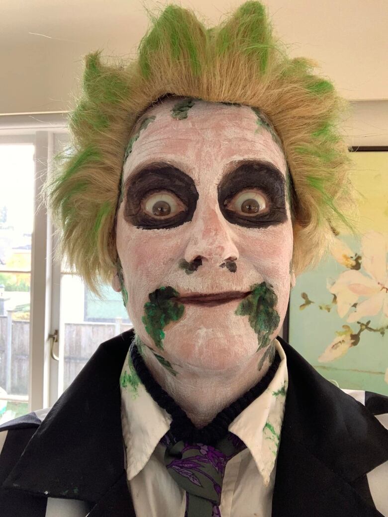 A woman dressed up as beetlejuice, with white face paint and spiky green hair.