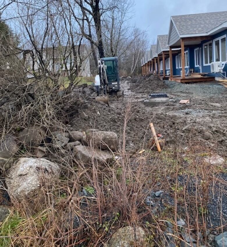 A small excavator sits on the left side of the property line, on Broussard's land, appearing to move earth as piles of infilling sit beside it.