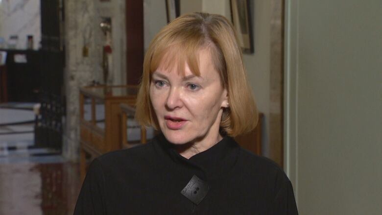 A white woman with red hair and a black jacket stands in a hallway.