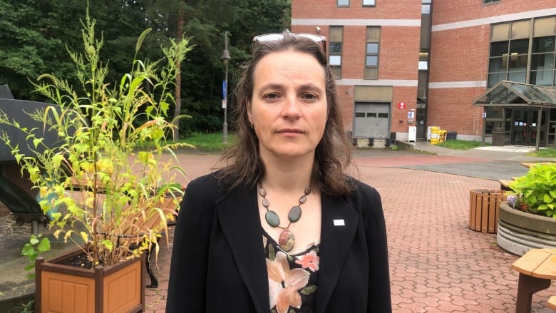 A woman looks directly at the camera standing outside a building