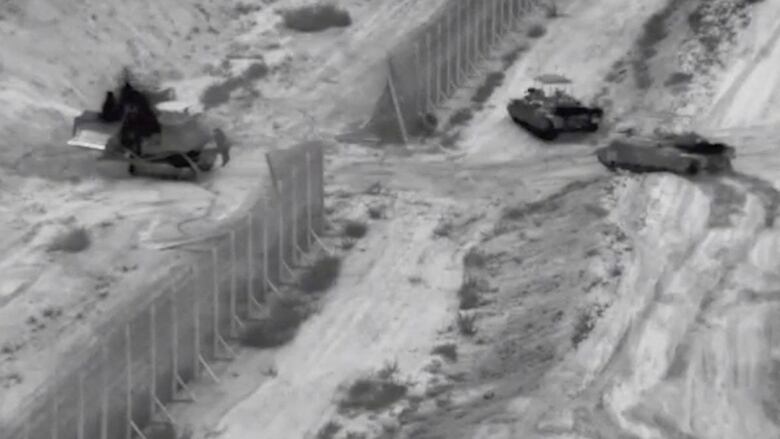 A row of tanks is seen from above advancing on a road