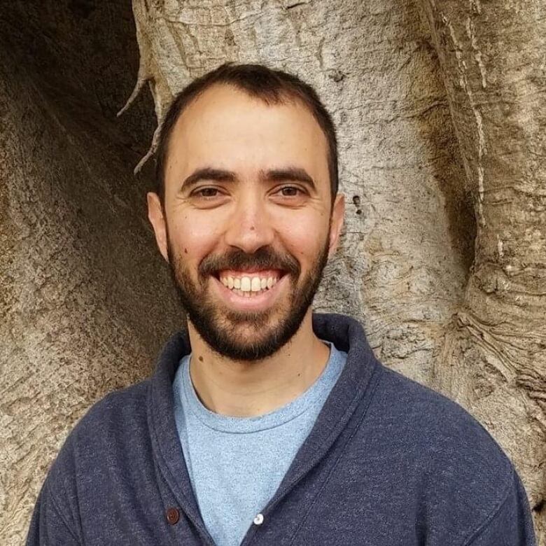 Portrait of a smiling bearded man in front of a tree.