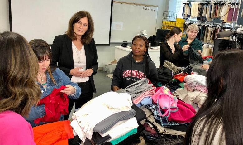 A woman looks at a crowd sorting through piles of colourful clothing.