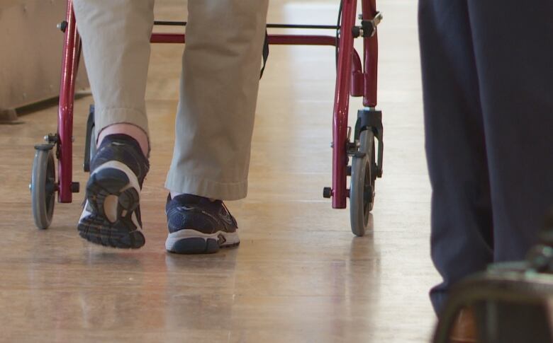 A pair of feet clad in sneakers are visible as someone uses a walker to move down a shiny hallway.