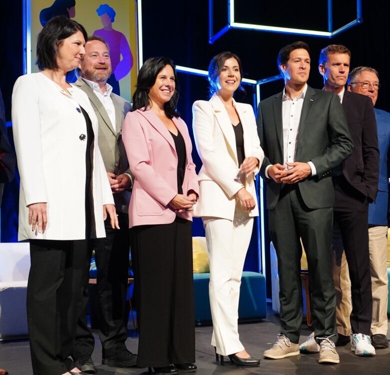 Group of men and women in suits line up for a photo on a stage.