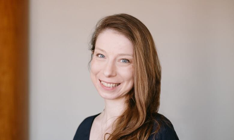 A woman with pale skin, blue eyes and strawberry blonde hair wearing a black top smiles for a photo.