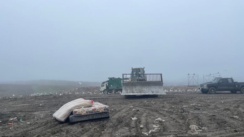 Discarded mattresses in a landfill about to be processed by an operator.