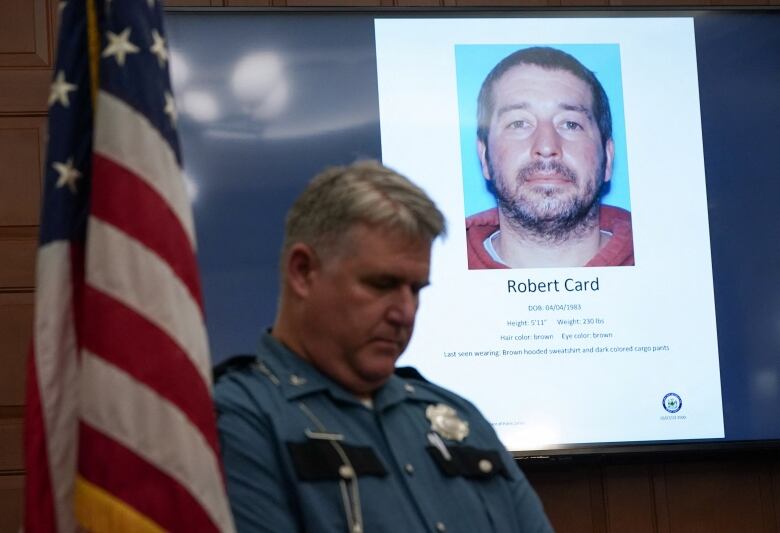 A police officer stands in front of a TV screen displaying a picture of a suspect.