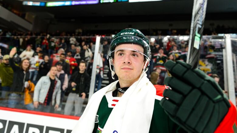 A hockey player tips his stick to the crowd, who are shown cheering him on.