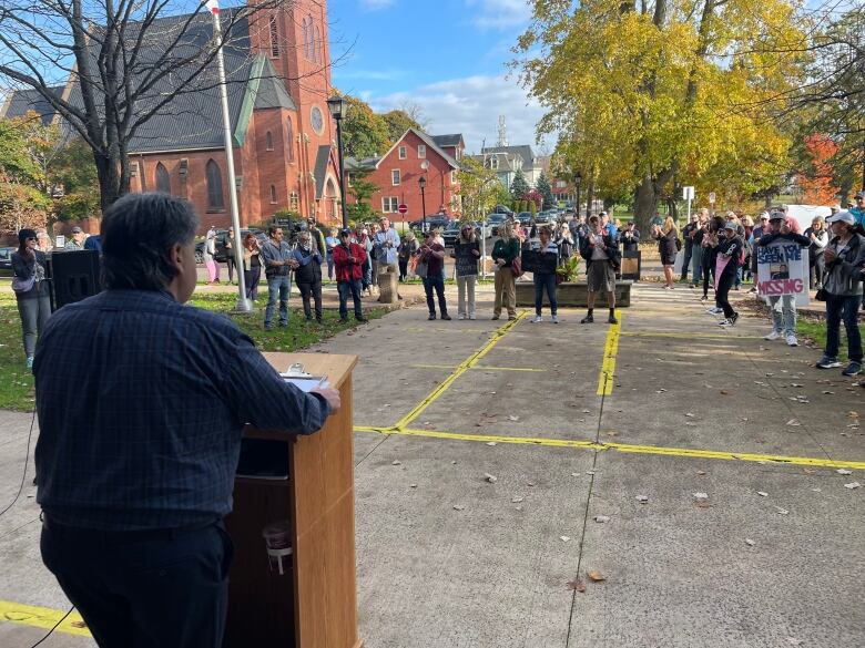 A man speaks at a podium to a crow of protesters outside a government building in Charlottetown. 